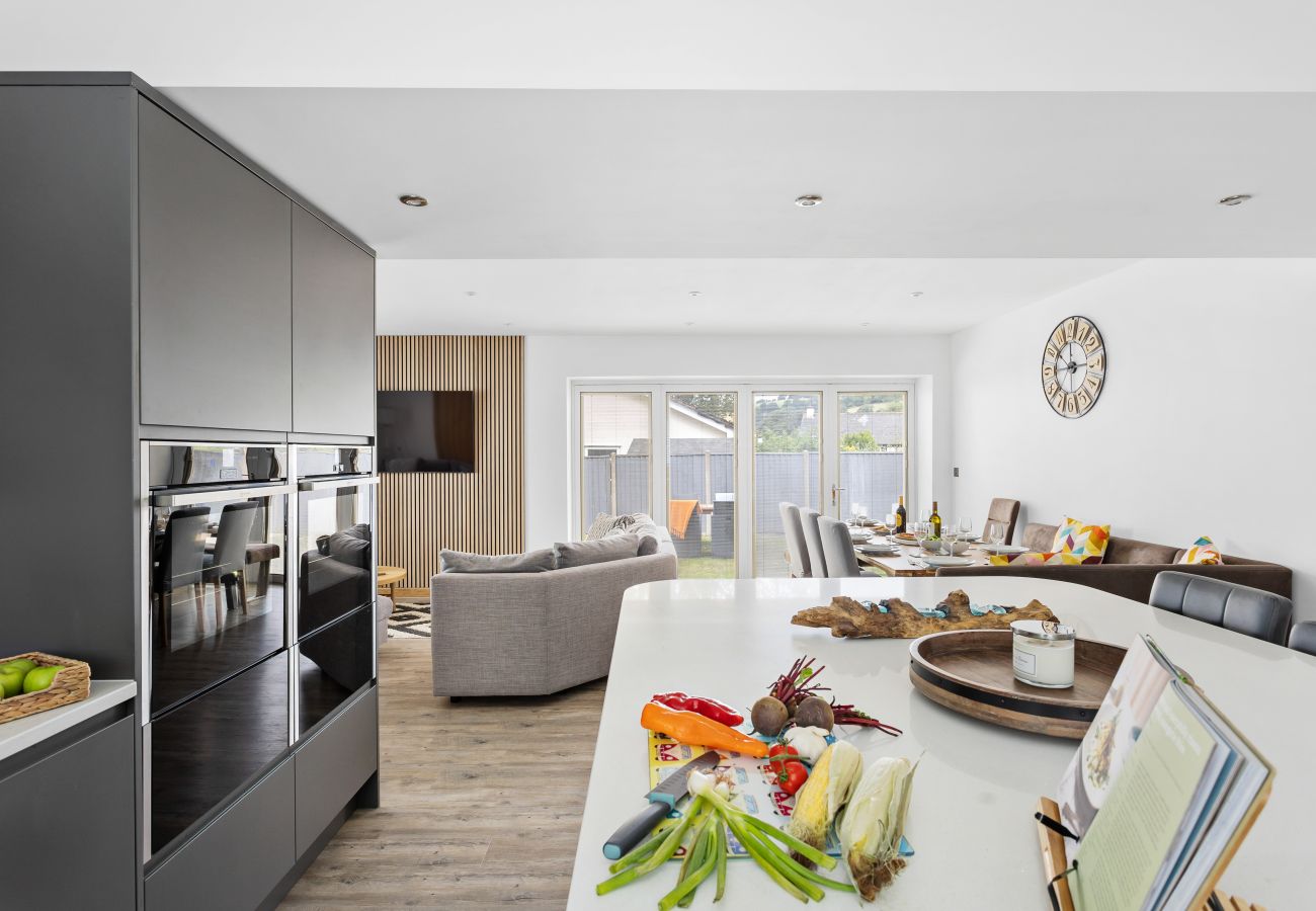 Spacious open-plan living area with curved sofas and bi-fold doors leading to a garden seating area.